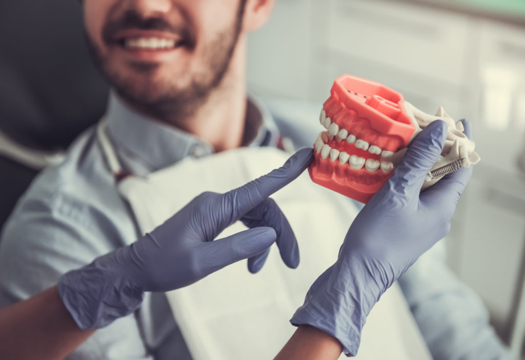 Dentista mostra molde dentário para paciente para falar das restaurações que melhoram a oclusão no tratamento contra bruxismo.