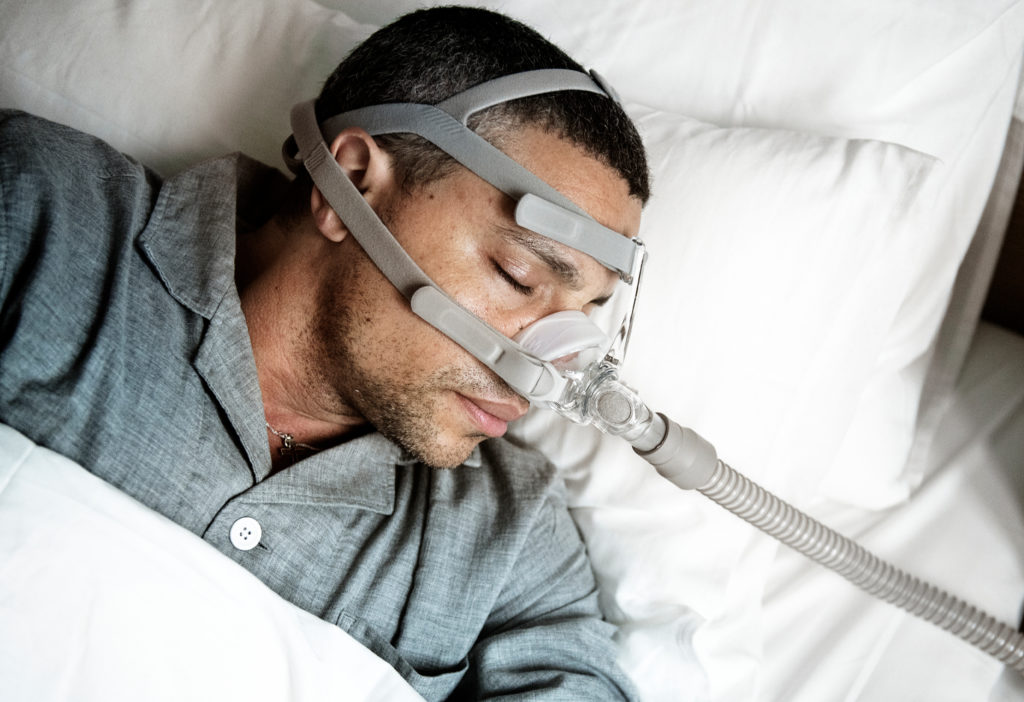 Homem utilizando o CPAP: uma opção da odontologia do sono para auxiliar a abertura das vias respiratórias e garantir noites de sono tranquilas.